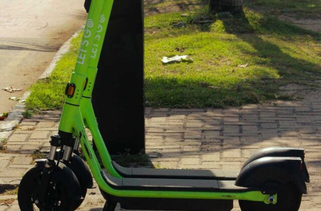 A shared electric scooter parked on a busy boulevard sidewalk at dusk