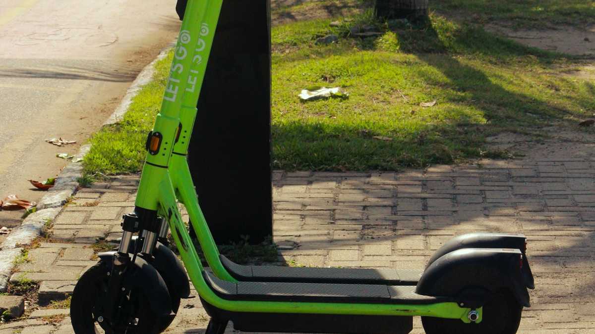 A shared electric scooter parked on a busy boulevard sidewalk at dusk
