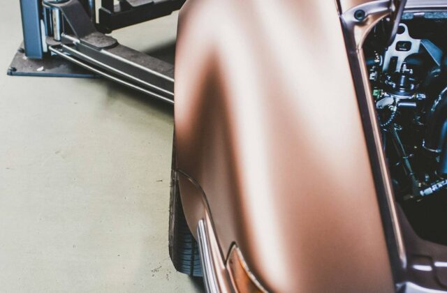 A car raised in a workshop with aftermarket wheels visible on the shop floor