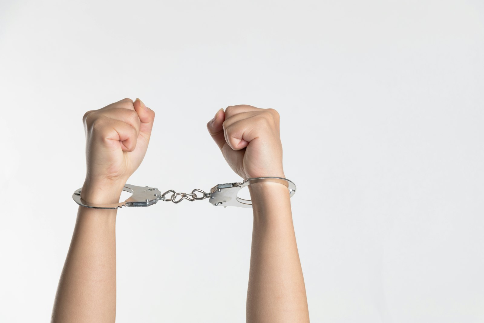Person's raised hands showing a pair of metal handcuffs against a plain background