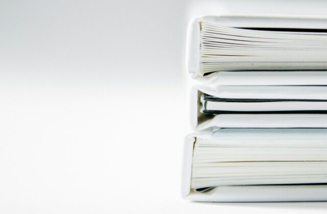 Stack of thick white document binders and folders on a plain white surface