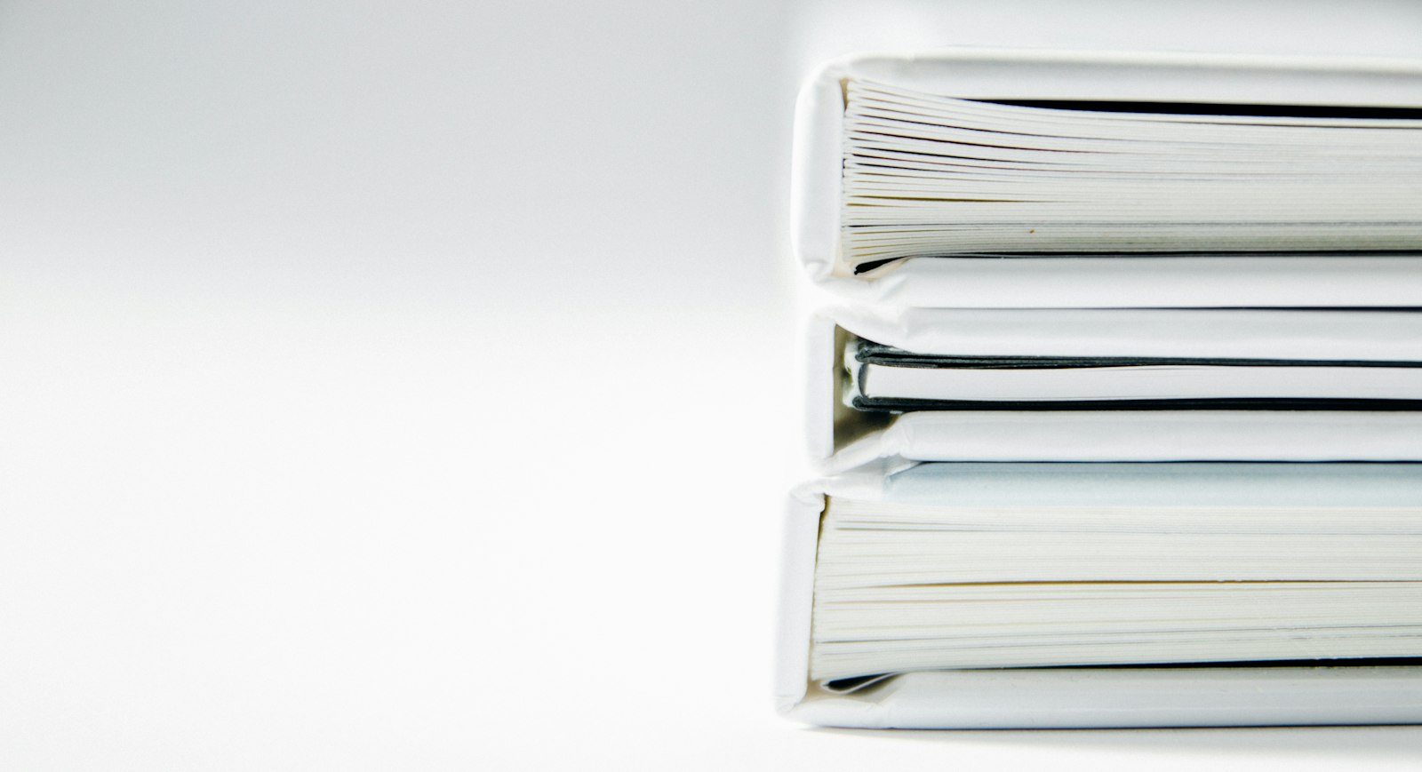 Stack of thick white document binders and folders on a plain white surface