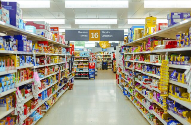 Supermarket aisle with shelves stocked with packaged snacks and overhead signs