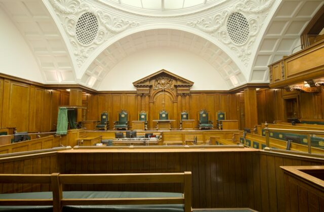 Empty courtroom with rich wooden paneling and a decorative ceiling