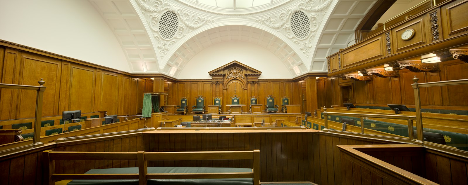 Empty courtroom with rich wooden paneling and a decorative ceiling