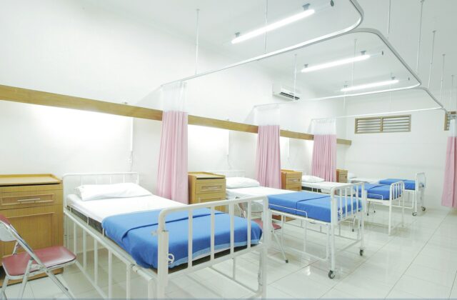 Empty hospital beds with pink curtains inside a bright patient ward