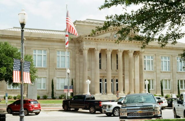 Classical government building with columns and American flags beside parked cars