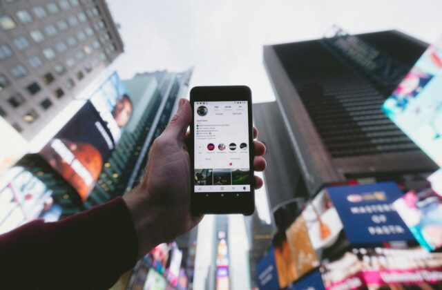 Hand holding a smartphone showing an Instagram profile against city buildings
