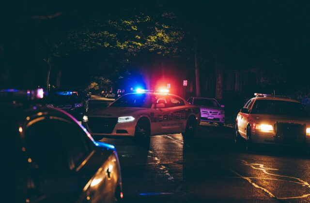 Police cars with flashing red and blue lights on a dark residential street