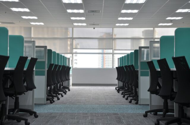 Rows of empty black rolling chairs at office cubicles with desktop computers